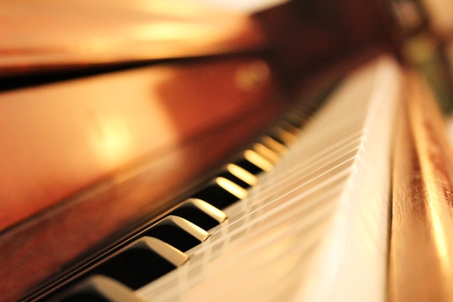Close-up view of piano keys, focusing on a shallow depth of field that highlights the glossy surface and elegant black and white keys. The warm wooden frame provides a soft, inviting glow.