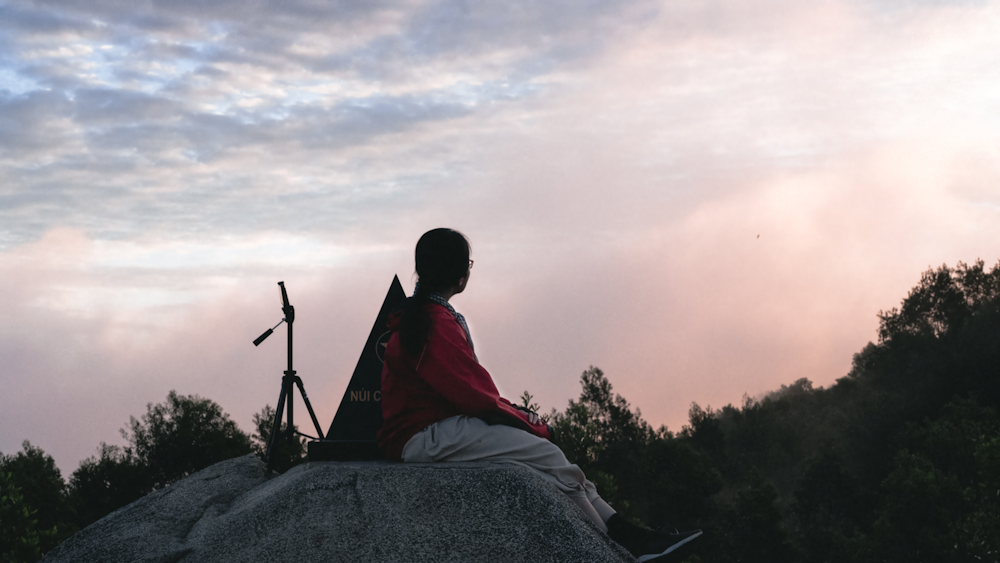 a man sitting on top of a rock next to a rifle