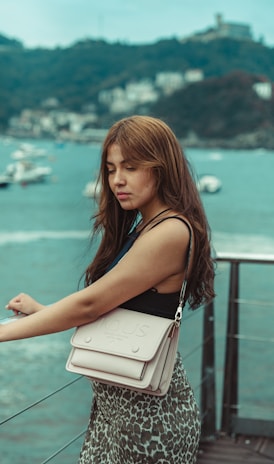 a woman holding a white purse on top of a pier