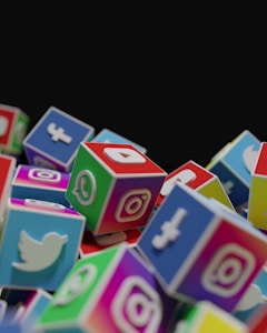 A collection of colorful cubes stacked together, each with the logo of a popular social media platform such as Twitter, Instagram, Facebook, and WhatsApp. The cubes are arranged in a way that they appear to be tumbling or piled up.