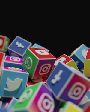 A collection of colorful cubes stacked together, each with the logo of a popular social media platform such as Twitter, Instagram, Facebook, and WhatsApp. The cubes are arranged in a way that they appear to be tumbling or piled up.