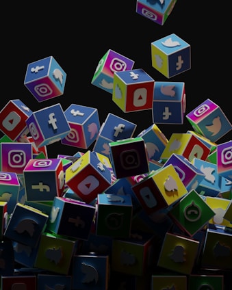 A collection of colorful 3D cubes displaying logos of various social media platforms, including Facebook, Instagram, Twitter, YouTube, and others. The cubes appear to be falling and tumbling over each other against a dark background.