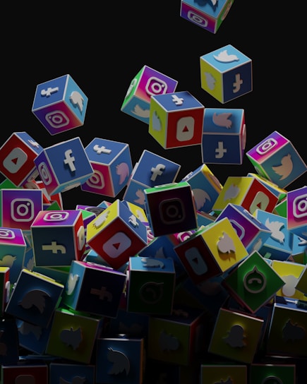 A collection of colorful 3D cubes displaying logos of various social media platforms, including Facebook, Instagram, Twitter, YouTube, and others. The cubes appear to be falling and tumbling over each other against a dark background.