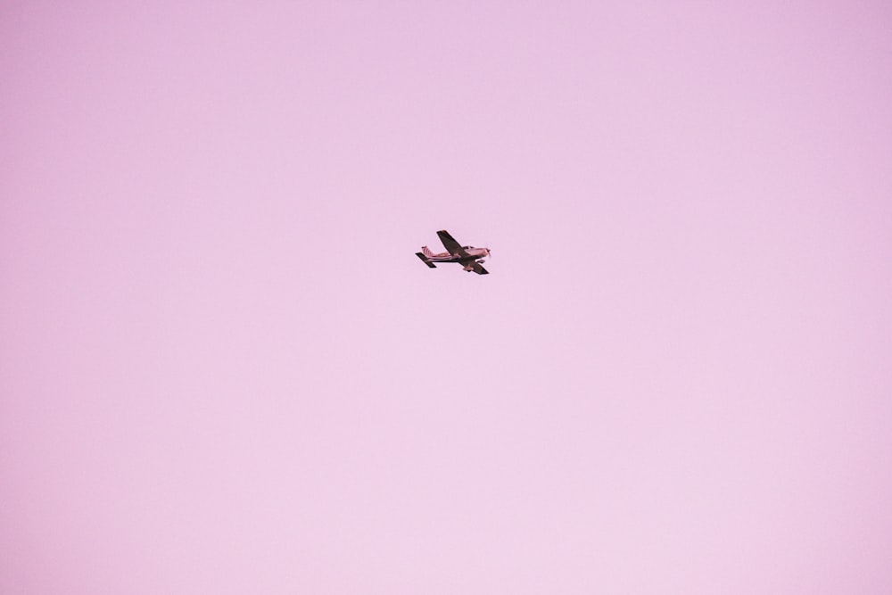 a small plane flying through a pink sky
