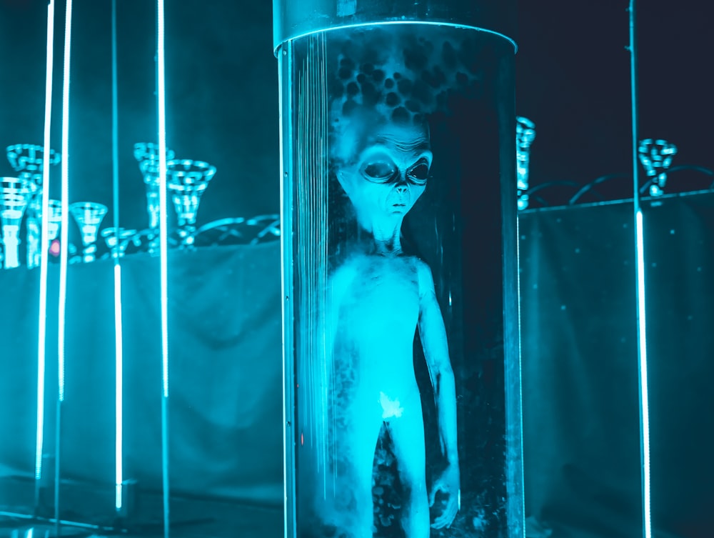 an alien doll is standing in a glass tube
