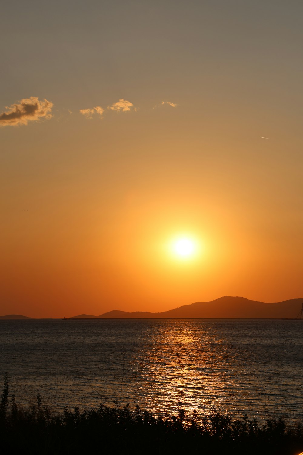 the sun is setting over the ocean with a sailboat in the distance