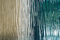 A close-up of a textured surface with flowing vertical lines resembling wood grain patterns, featuring a blend of earthy beige and deep teal colors.