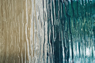 A close-up of a textured surface with flowing vertical lines resembling wood grain patterns, featuring a blend of earthy beige and deep teal colors.
