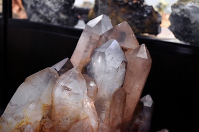 A cluster of large, clear crystal formations with distinct pointed tips is prominently displayed. The crystals exhibit a range of natural hues from transparent to light brown, with some earthy inclusions visible within. The lighting emphasizes the facets and angles of the crystals, creating reflections and subtle color variations.
