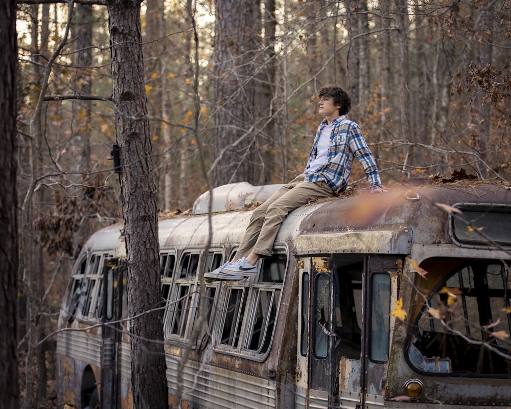 a man sitting on top of an old bus in the woods