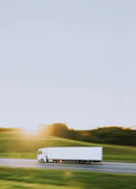 a white truck driving down a road next to a lush green field