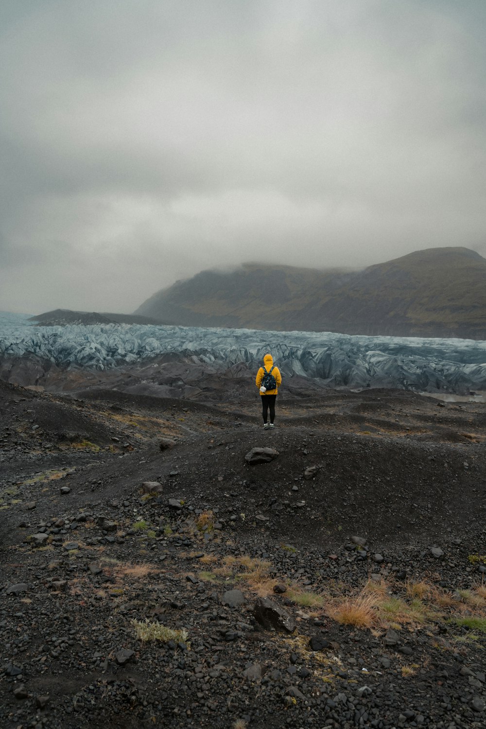 a man in a yellow jacket standing on a rocky beach