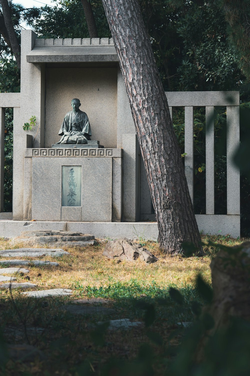 a statue of a man sitting in front of a tree