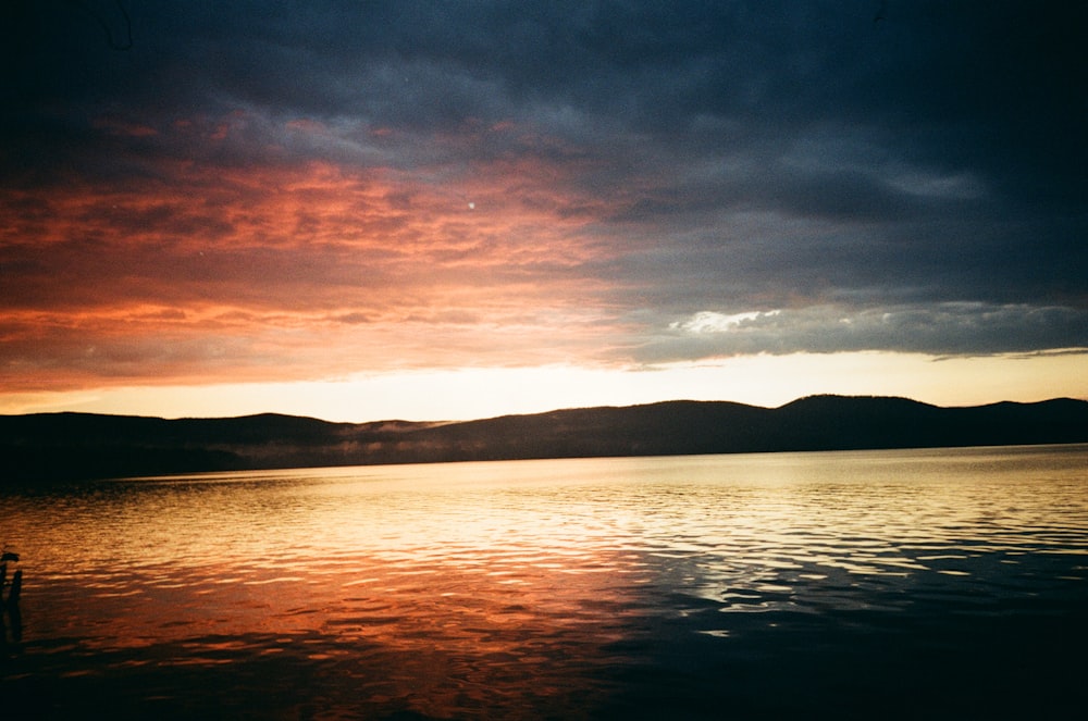 a sunset over a body of water with mountains in the background