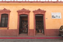 A small bookstore with two open doorways leading to shelves filled with books. The building has a rustic yellow facade with reddish-brown trim and architectural details. A sign next to the doorway reads 'Librer&iacute;a No 1 Barco de Papel' advertising book sales.