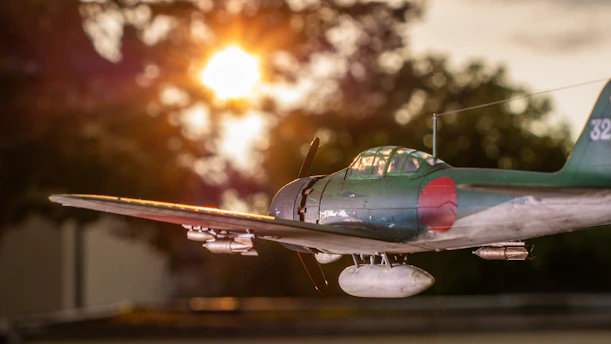A vintage World War II fighter plane soaring over a dramatic battlefield landscape at sunset.