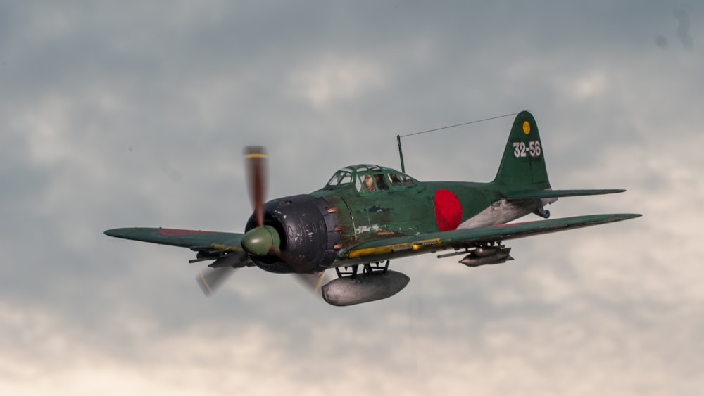 a small green airplane flying through a cloudy sky