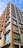 A modern multi-story building with large glass windows and wooden paneling provides a sleek architectural design. The structure reaches up into the clear blue sky, creating an impression of height and contemporary style.