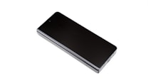A closed black foldable smartphone with a sleek, reflective surface, lying flat on a white background. The edges are metallic, and a camera lens is visible at the top edge.