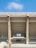 A large concrete structure with multiple levels and prominent support beams is visible under a clear blue sky. The architecture includes open spaces and railings, suggesting it is part of a stadium or similar building.