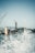 Cranes are positioned above a large industrial shipyard, with a dock and a partially visible ship. Water sprays in the foreground, adding a dynamic effect to the scene.