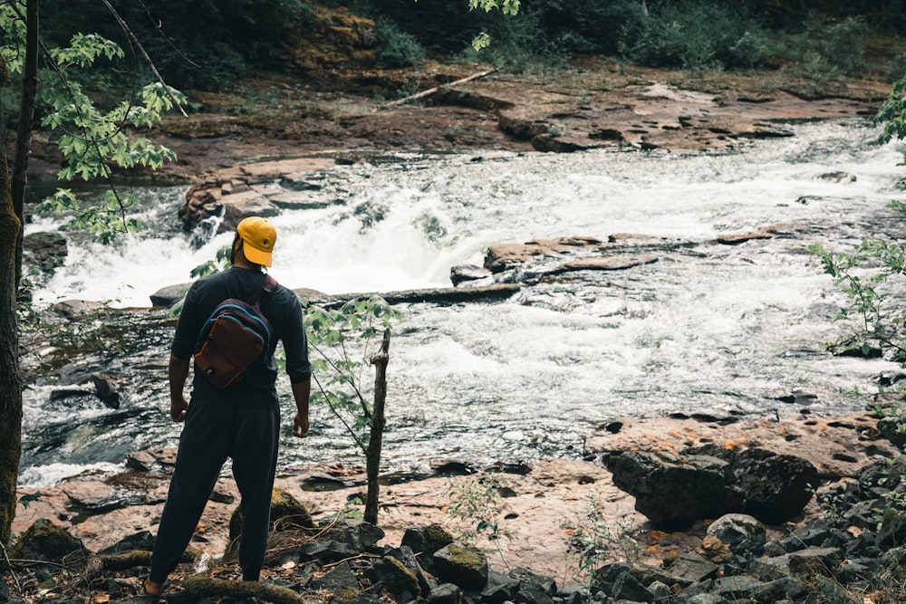 a man with a backpack standing on rocks near a river