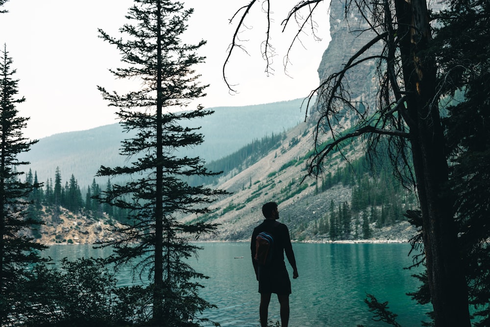 a man standing on the edge of a lake surrounded by trees