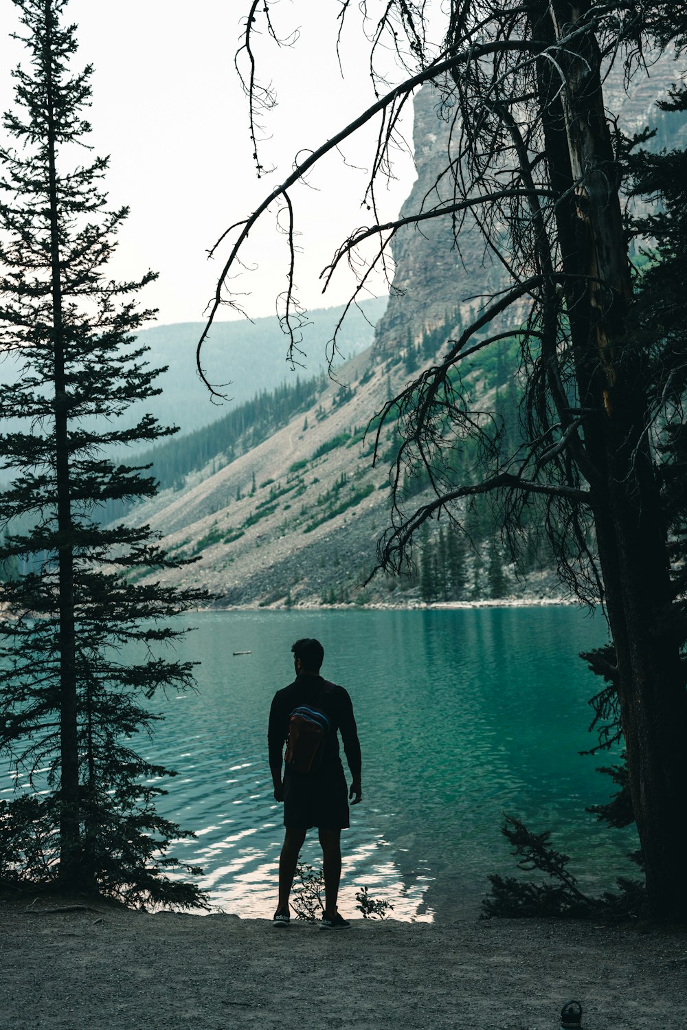 a man standing in front of a lake surrounded by trees