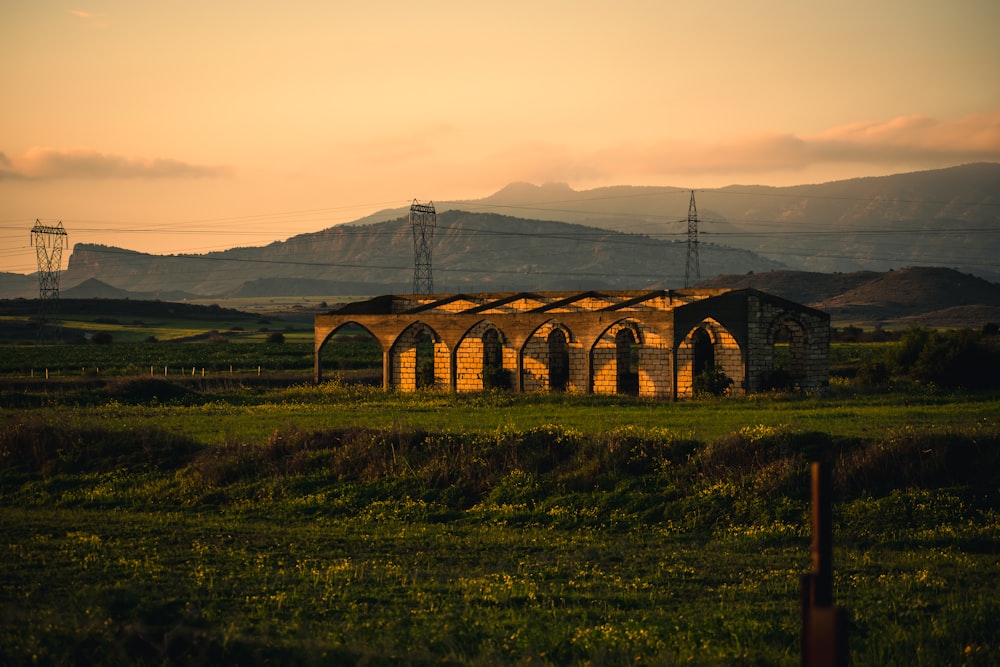 an old building in a field with mountains in the background