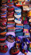 An assortment of small, colorful fabric pouches and wallets with various designs are arranged on display. Many of the items feature vibrant stripes and patterns, some include text such as 'El Salvador'. The items appear to be made of woven textiles and leather accents, showcasing craftsmanship and cultural motifs.