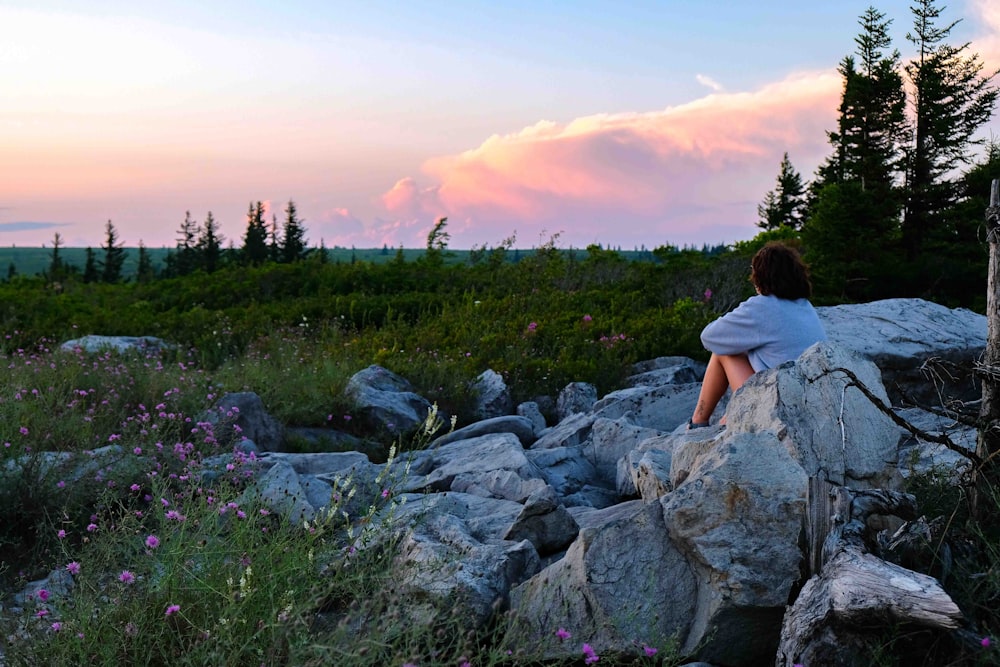 a woman sitting on top of a large rock