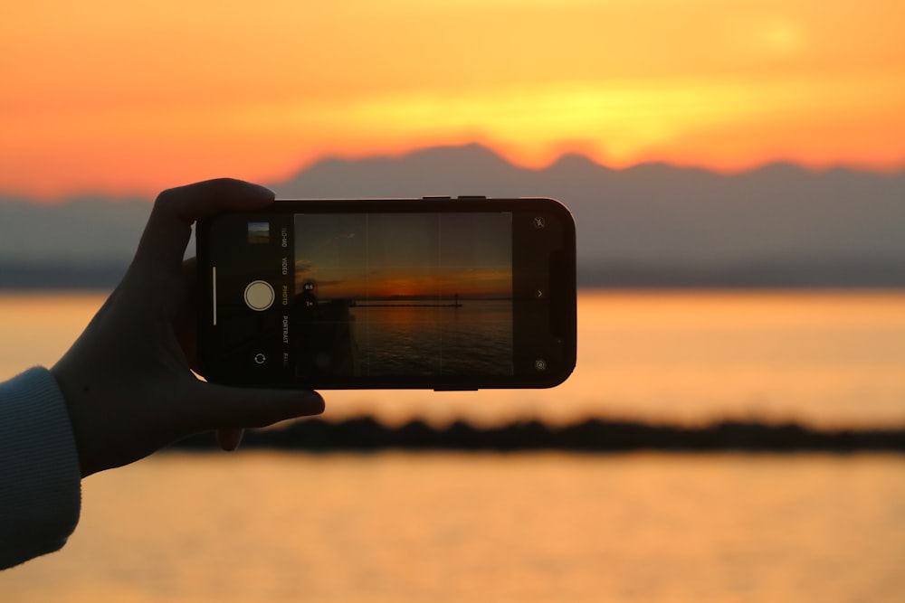 a person taking a picture of a sunset with a cell phone