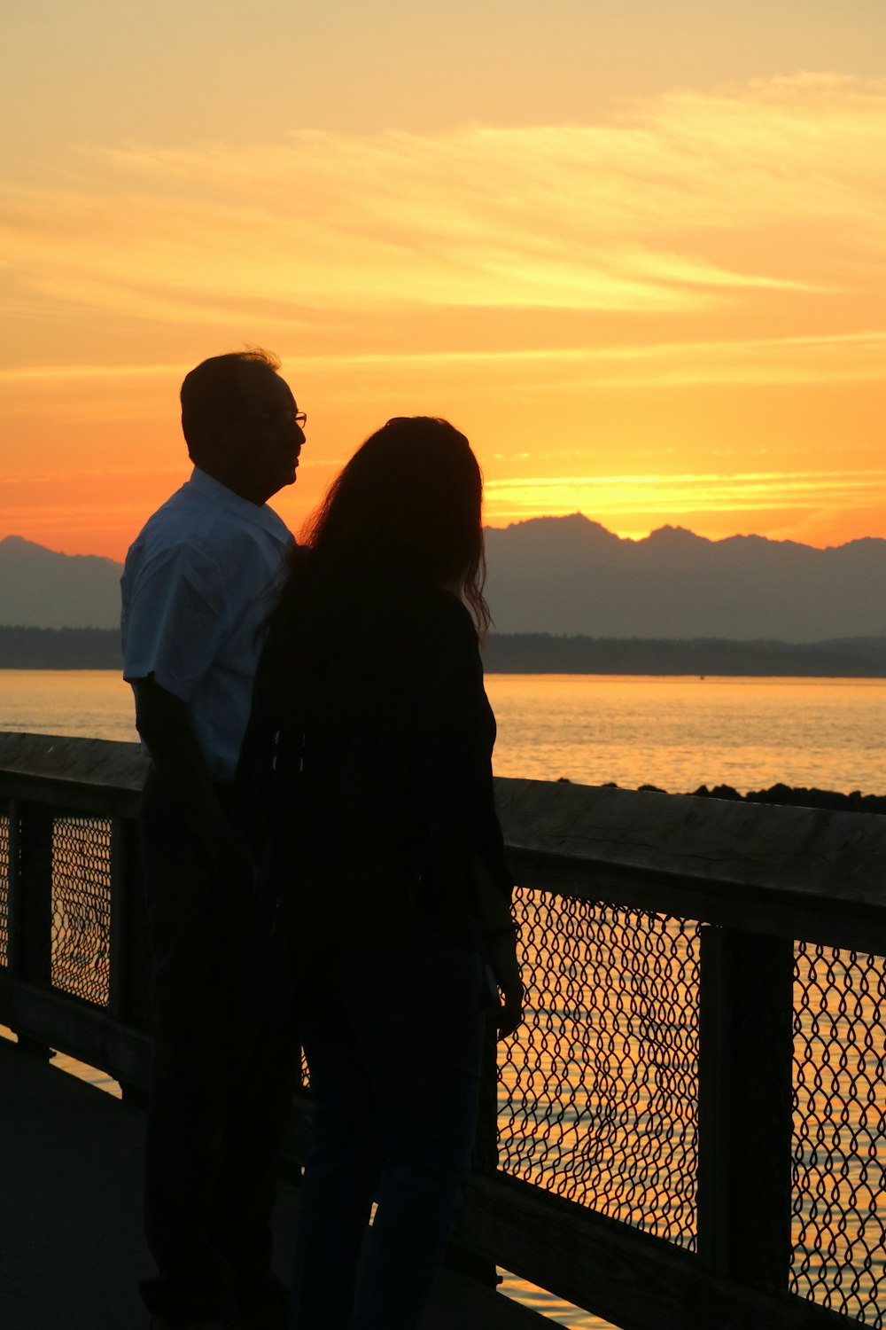 a man and a woman standing on a pier watching the sunset