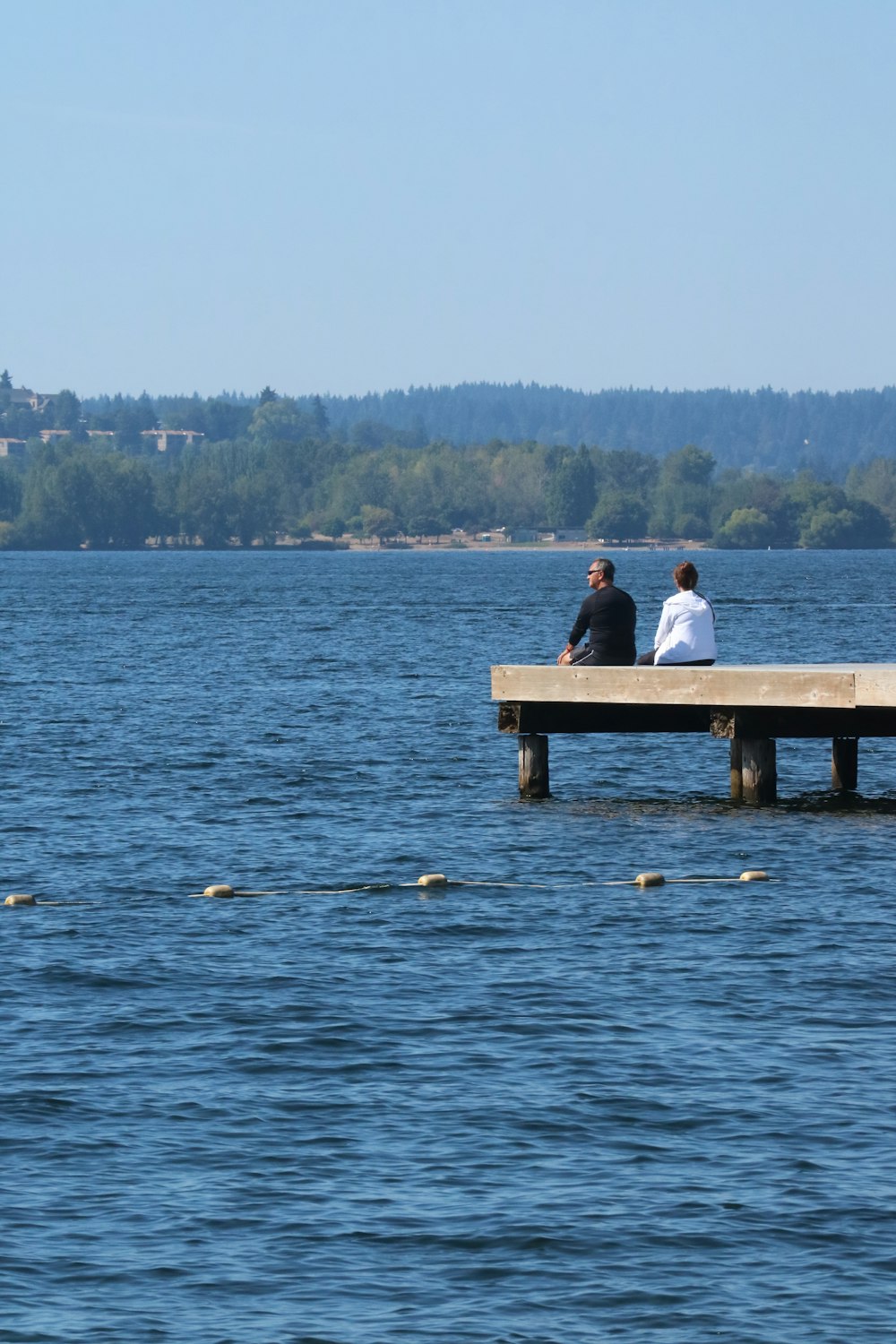 two people sitting on a dock in the middle of a lake