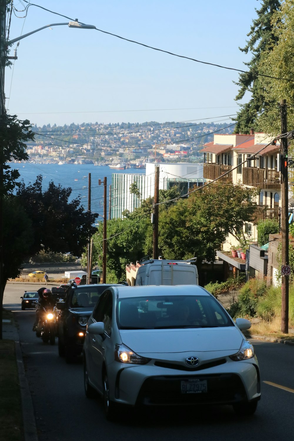 a white car driving down a street next to a lush green hillside