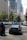 A busy city street scene with several cars and a motorcycle in traffic. In the background, tall modern buildings with reflective glass facades and a banner for the Seattle Art Museum are visible. Trees line the street, adding some greenery to the urban setting.