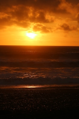 A vibrant sunset over a serene beach with golden sands and dark blue waves.