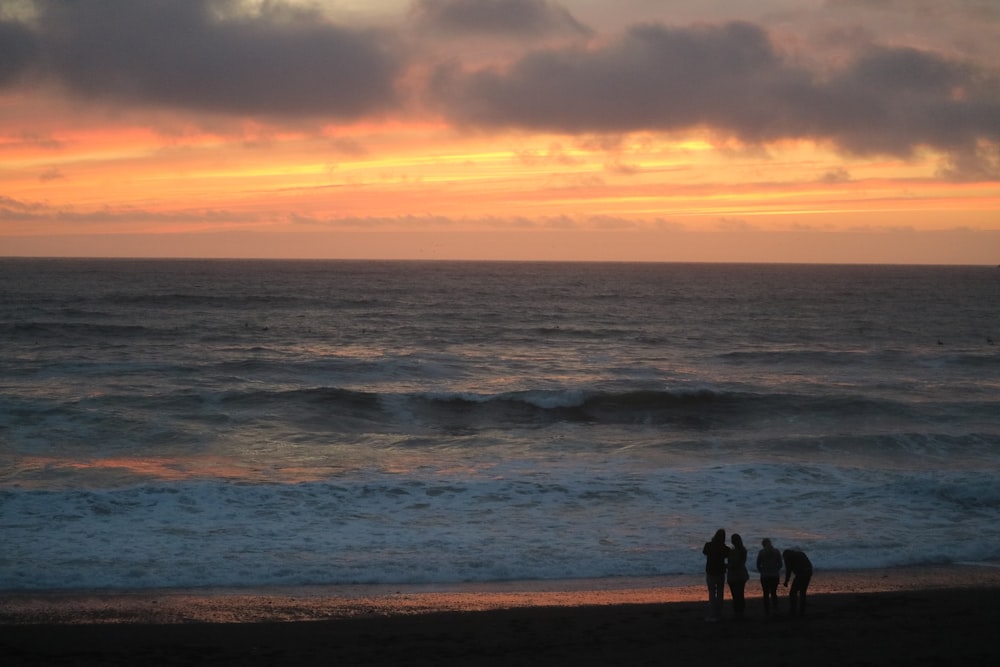 a group of people standing on top of a beach next to the ocean