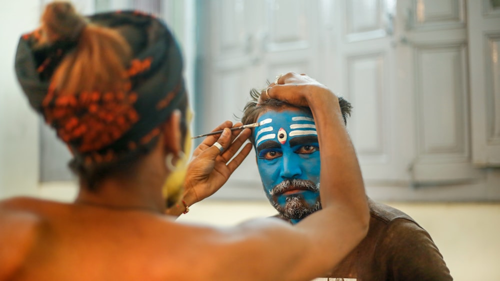 a man getting his face painted in blue