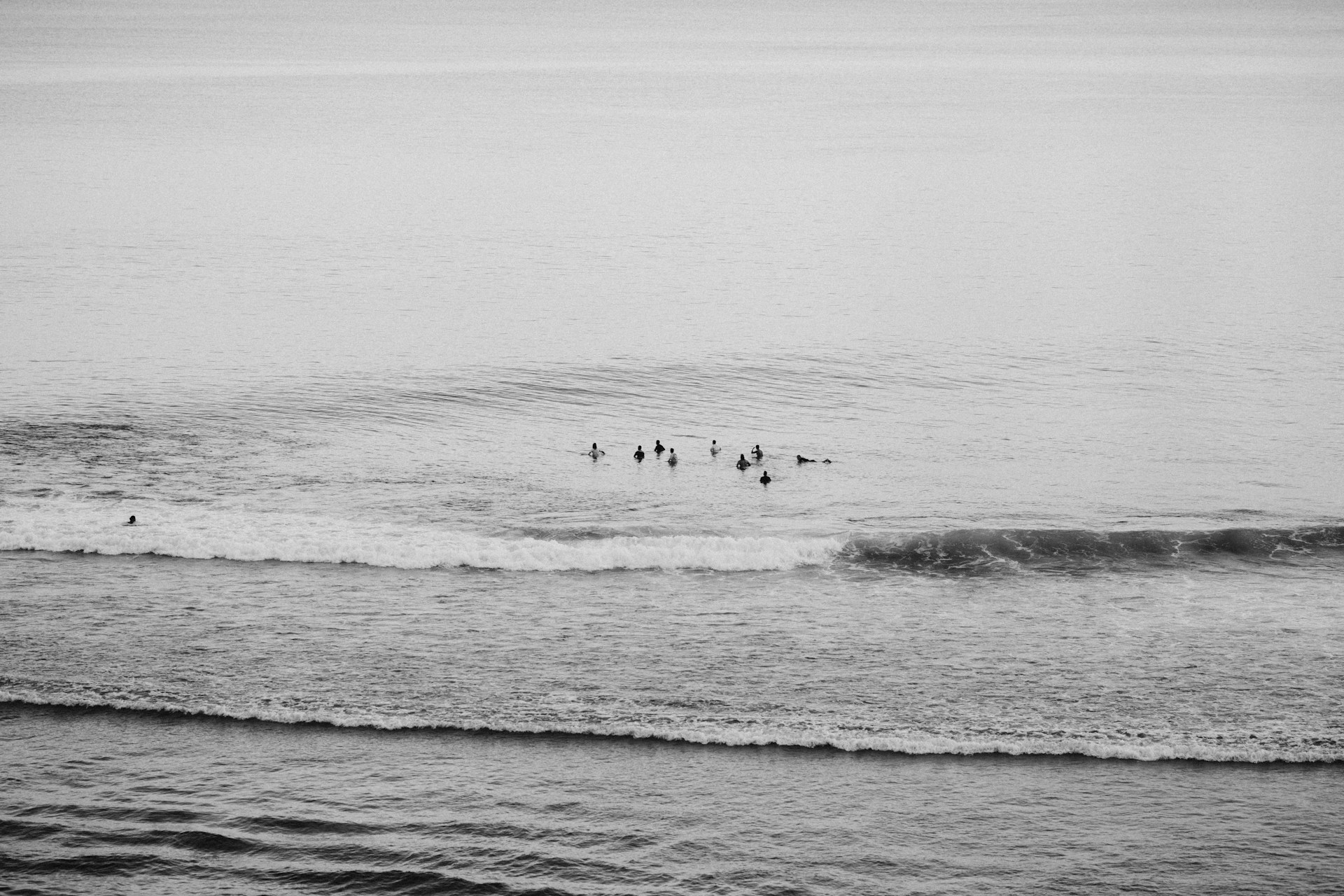 A panoramic shot of a beach with surfers waiting for waves, capturing the calm before the action.
