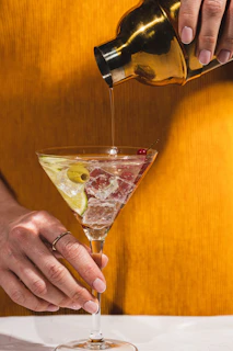 A gold-accented shaker mid-pour, sending a cascade of a sparkling cocktail into a chilled glass.