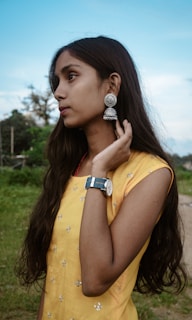 A model wearing colorful earrings with a vibrant summer dress in a sunny park.