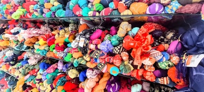 Rows of neatly arranged colorful fabric rolls fill the shelves with a wide range of patterns and textures. The fabrics are tightly packed, displaying a rich array of colors including reds, blues, greens, yellows, and purples. Each roll appears unique, contributing to a vibrant, visually appealing tapestry.