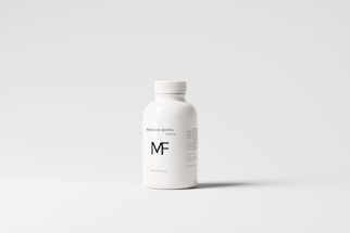 A white plastic bottle with a screw top, labeled 'Medicine Bottle mockup' and the letters 'MF' in bold. The bottle is placed against a plain, light gray background, with some small text details visible on the right side.