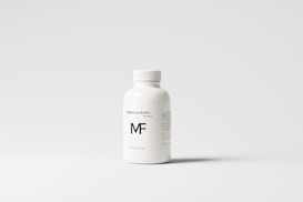 A white plastic bottle with a screw top, labeled 'Medicine Bottle mockup' and the letters 'MF' in bold. The bottle is placed against a plain, light gray background, with some small text details visible on the right side.