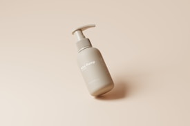 A gray pump bottle labeled 'Mini Pump' lies on its side against a smooth, beige background. The bottle has a sleek design and appears to be made for skincare or personal hygiene products.