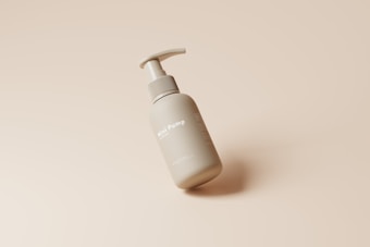 A gray pump bottle labeled 'Mini Pump' lies on its side against a smooth, beige background. The bottle has a sleek design and appears to be made for skincare or personal hygiene products.