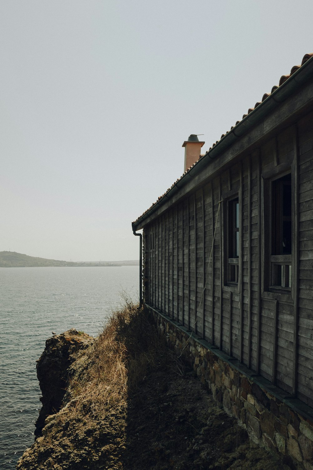 an old wooden building sitting on top of a cliff next to a body of water