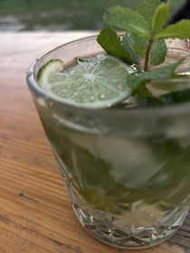 A vibrant glass of iced hibiscus tea garnished with a slice of lime and mint leaves on a sunny patio.