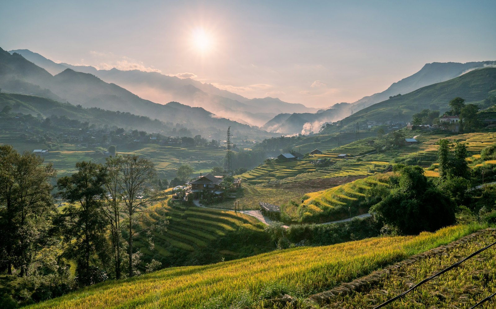 Terraced rice fields stepping down a valley near Sapa with mountains and a hazy sun behind
